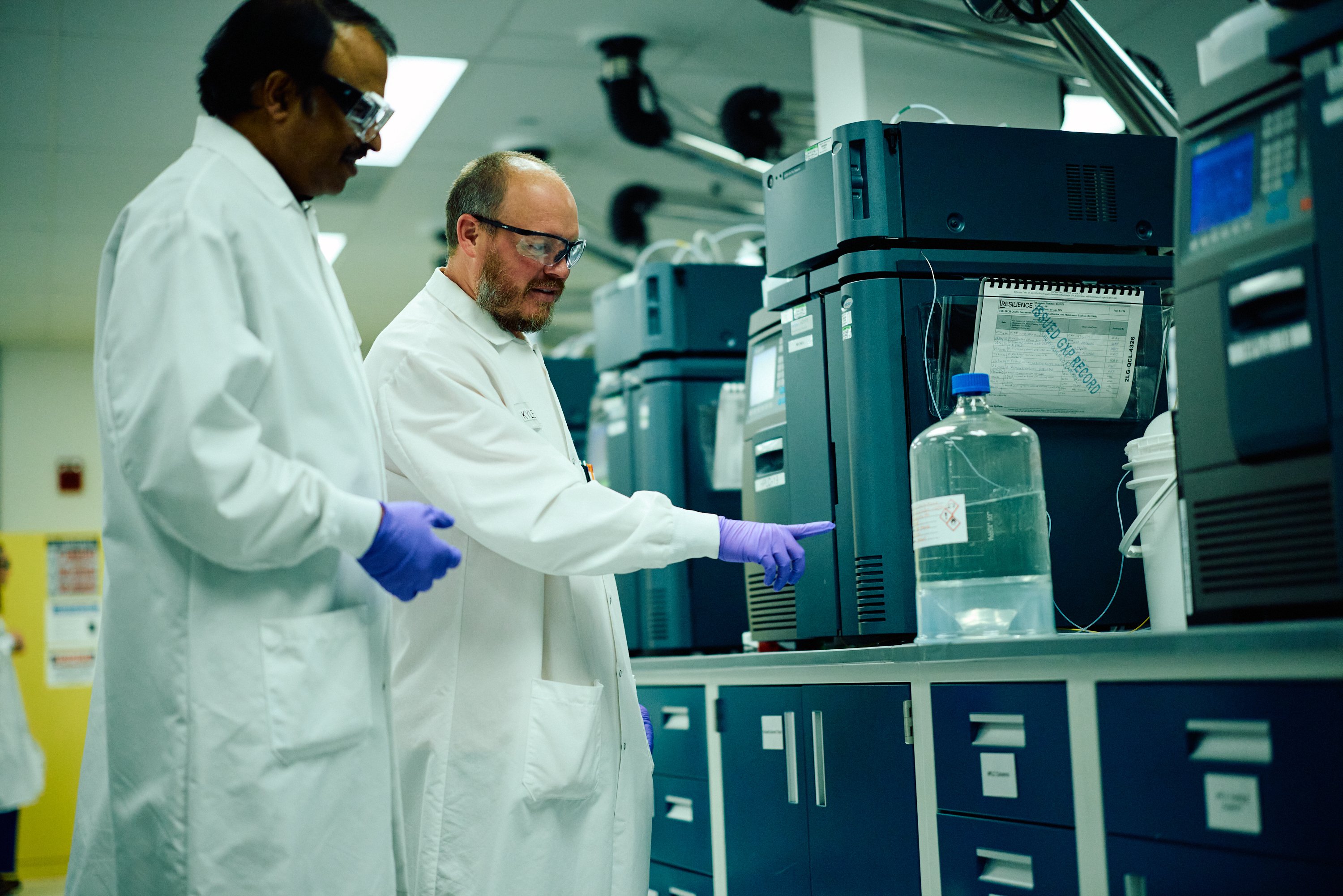 Two laboratory researchers examining analytical testing machinery in a lab.