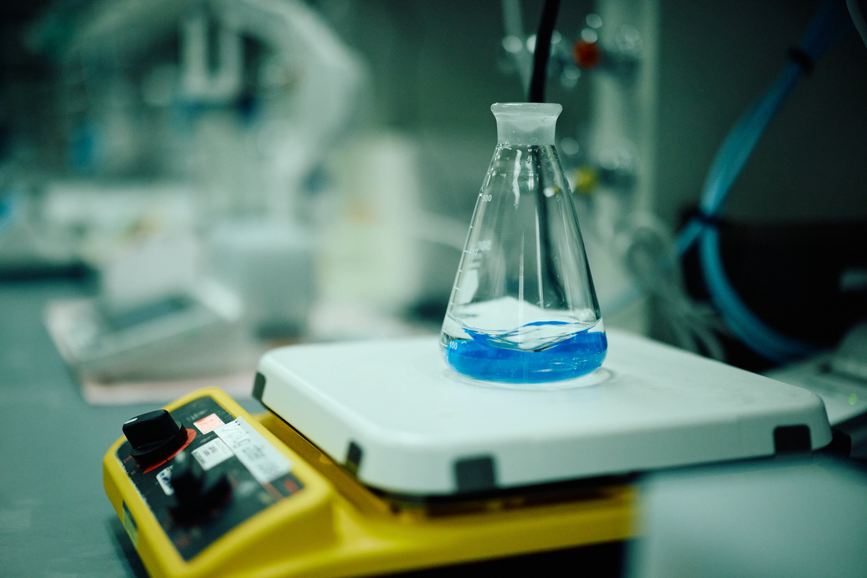 Glass flask filled with blue liquid on a laboratory hot plate stirrer.