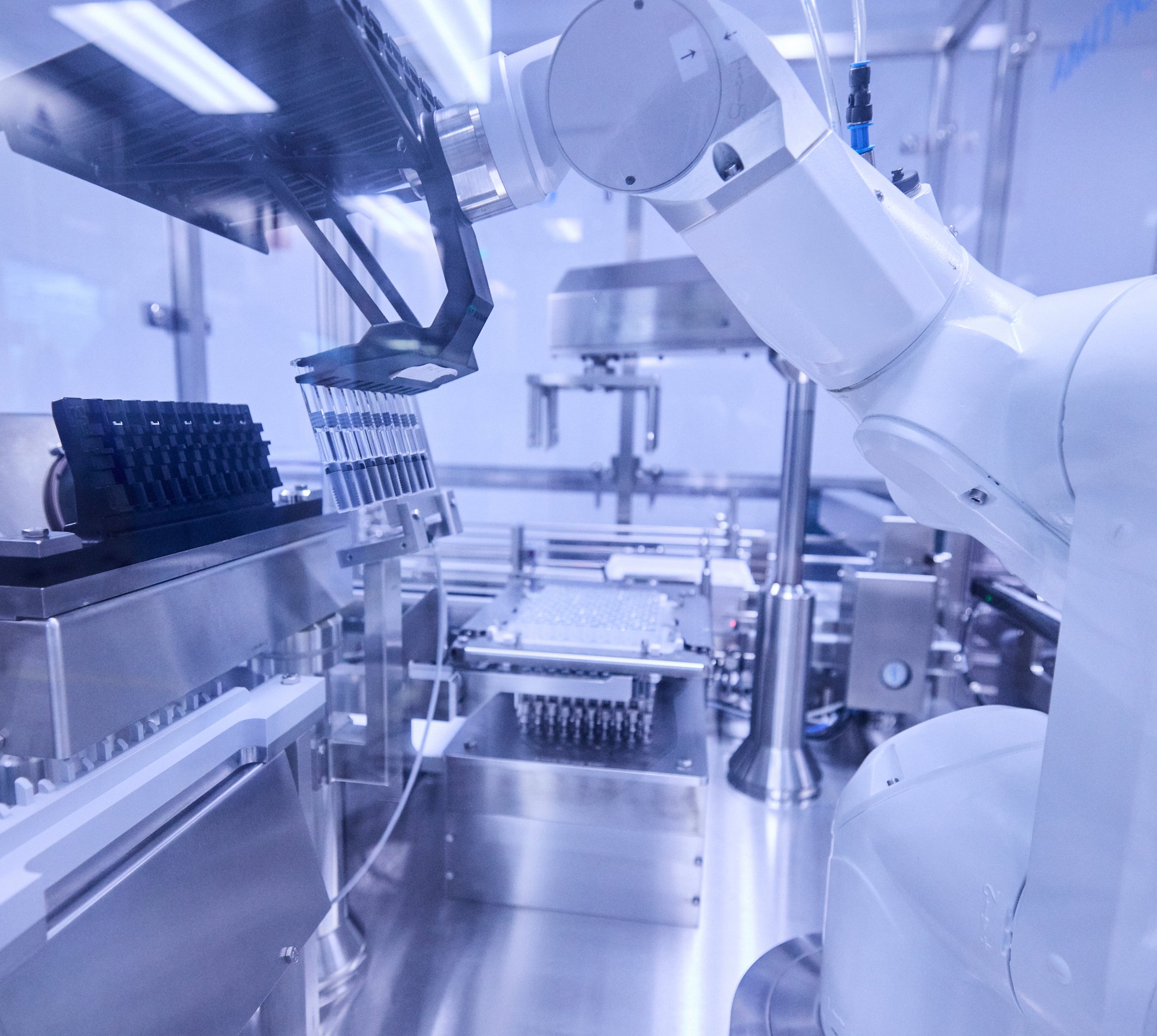 Automated robotic arm holding a row of vials inside a sterile laboratory enclosure.