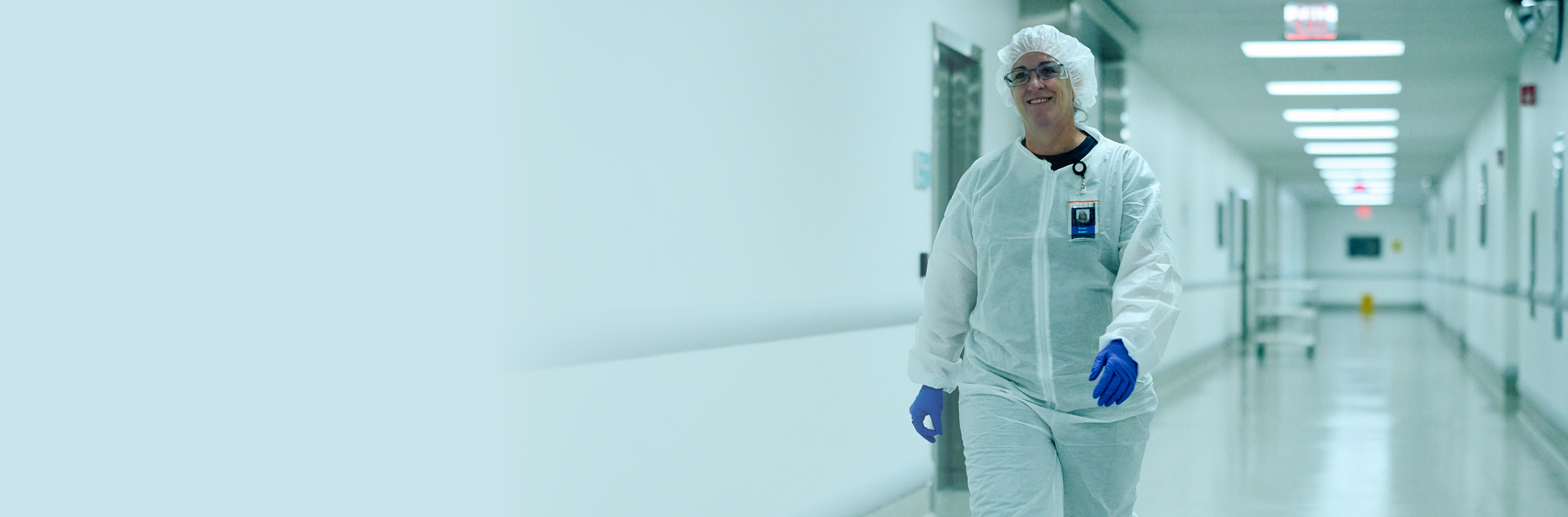 Laboratory worker in a protective cleanroom jumpsuit walking through a facility corridor