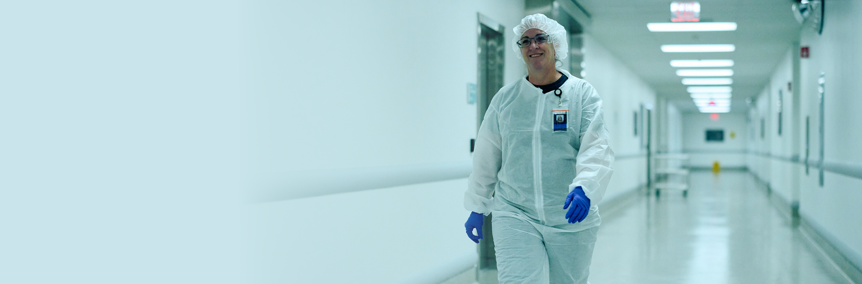 Laboratory worker in a protective cleanroom jumpsuit walking through a facility corridor